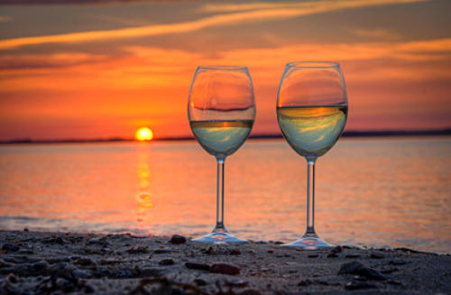 Zwei Weingläser am Strand vor einem Sonnenuntergang über dem Meer