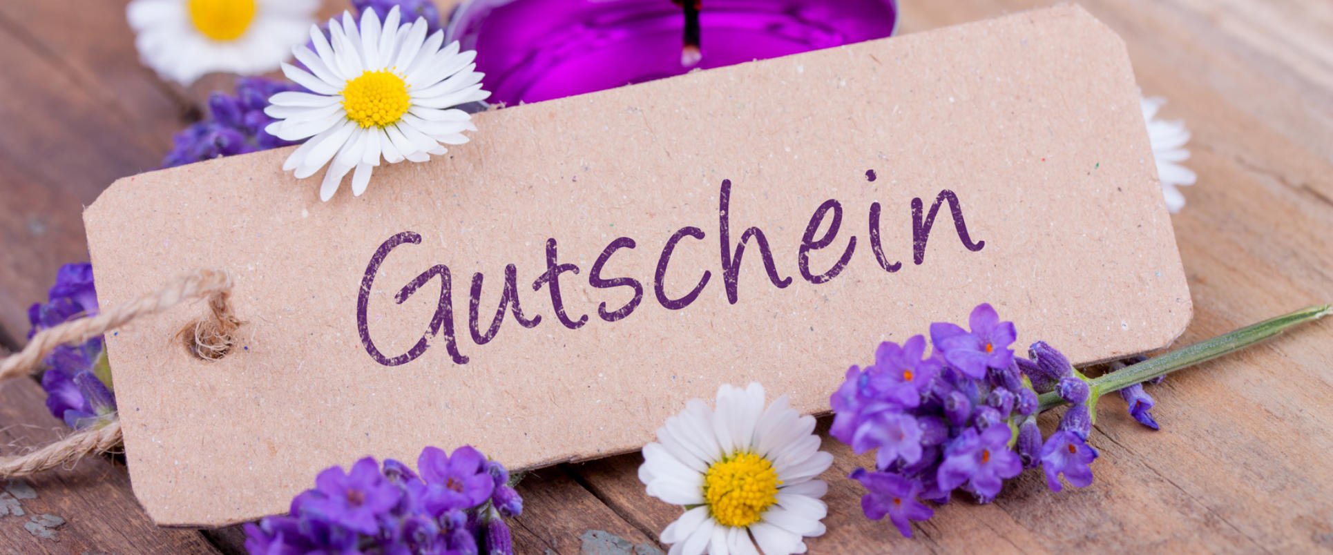 Geschenkanhänger mit der Aufschrift „Gutschein“ zwischen Lavendel, Gänseblümchen und einer Kerze