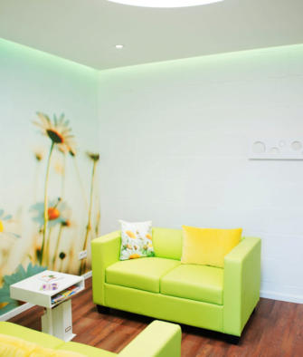 Heller Praxisraum mit hellgrünem Sofa, bunten Kissen und einer Blumenwiese als Wandbild